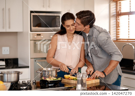 Cooking, couple and kiss on cheek in kitchen for love, romance and support at home. Man, woman and cutting vegetables on counter for dinner, date night and happiness in marriage in living space Cooking, couple and kiss on cheek in kitchen for love, romance and support at home. Man, woman and cutting vegetables on counter for dinner, date night and happiness in marriage in living space 142047270