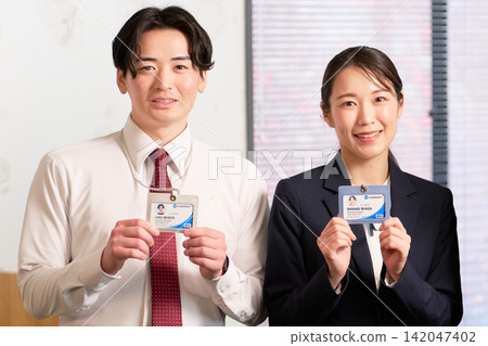 Young employees smiling and facing forward, holding their ID cards. Young employees smiling and facing forward, holding their ID cards. 142047402