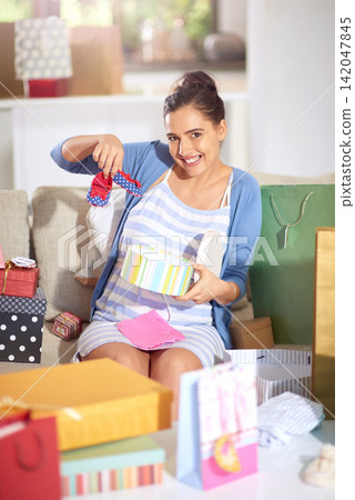 Woman, shoes and gift at baby shower for celebration, congratulations and excited with new clothes at home. Portrait of pregnant mother, mom or parent with present and unboxing on sofa in living room Woman, shoes and gift at baby shower for celebration, congratulations and excited with new clothes at home. Portrait of pregnant mother, mom or parent with present and unboxing on sofa in living room 142047845