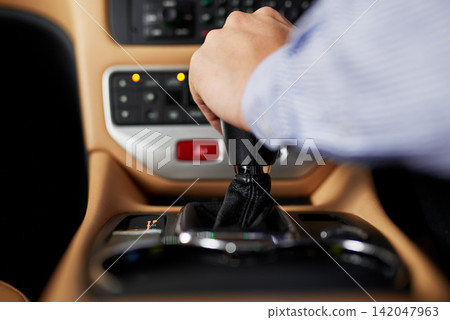 Hands, center console and gear of car for shift, transmission and speed change for driving or journey. Auto, stickshift and person in luxury automobile for clutch control, power and selector Hands, center console and gear of car for shift, transmission and speed change for driving or journey. Auto, stickshift and person in luxury automobile for clutch control, power and selector 142047963