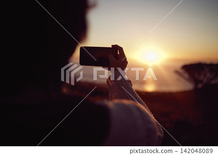Hiking, photography and woman with phone at sunset, nature and mountain to relax on holiday adventure. Smartphone, trekking and person with view of orange sky, ocean and memory on vacation from back Hiking, photography and woman with phone at sunset, nature and mountain to relax on holiday adventure. Smartphone, trekking and person with view of orange sky, ocean and memory on vacation from back 142048089