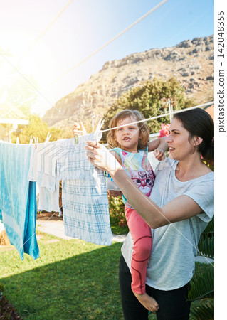 Backyard, mom and child hanging laundry together with help, teaching and learning chores. Housekeeping, mother and daughter with clean clothes on line outside to sun dry with home, care and bonding. Backyard, mom and child hanging laundry together with help, teaching and learning chores. Housekeeping, mother and daughter with clean clothes on line outside to sun dry with home, care and bonding. 142048355
