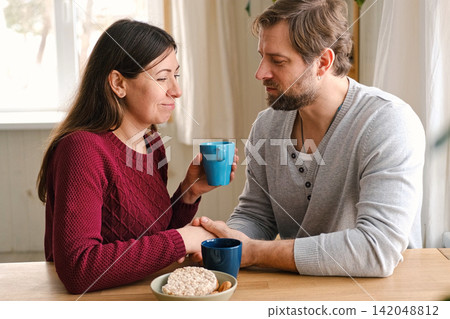 Loving mature couple interactions at home. Husband and wife hugging, holding hands and drinking morning coffee together. Man and woman talk about plans for weekend. Natural lighting. Intimate moments. Loving mature couple interactions at home. Husband and wife hugging, holding hands and drinking morning coffee together. Man and woman talk about plans for weekend. Natural lighting. Intimate moments. 142048812