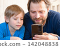 Father and son little boy laughing and using phone. They watching funny videos together, playing games on smartphone. Concept technology, smart phone addicted. Fun weekend activity. Modern fatherhood 142048838