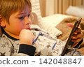 Cute kid boy in pajamas lying in bed watching smartphone, smiling. Children's screen time. Child plays games using phone at the evening or night. Social media addiction. Childhood, modern technology 142048847