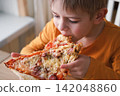 Cute healthy preschool kid boy eats a piece of cheese pizza for lunch. Charming child biting off big slice of fresh made pizza at the table in a restaurant indoor. Funny little toddler. Unhealthy food 142048860