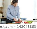 Close up of a woman chopping vegetables in a kitchen. Female hands cutting tomato, carrot on the board to preparing food. Then woman stir fried vegetables in a frying pan. Cooking in the kitchen 142048863