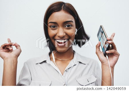 Phone, music and portrait of Indian girl with earphones in studio for dance, track or streaming audio on white background. Smartphone, app or gen z model smile for sign up playlist, radio or podcast Phone, music and portrait of Indian girl with earphones in studio for dance, track or streaming audio on white background. Smartphone, app or gen z model smile for sign up playlist, radio or podcast 142049059