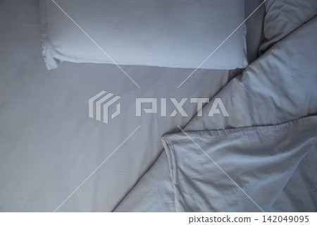 An overhead view of a bed with two pillows, covered with gray linens, lies a carelessly folded blanket, forming soft folds. The concept: an atmosphere of comfort and relaxation, going to bed. High 142049095