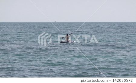 Novorossiysk Russia May 25 2026 Teenage boy paddling on a stand up paddleboard while kneeling in the Black Sea on a sunny day Novorossiysk Russia May 25 2026 Teenage boy paddling on a stand up paddleboard while kneeling in the Black Sea on a sunny day 142050572