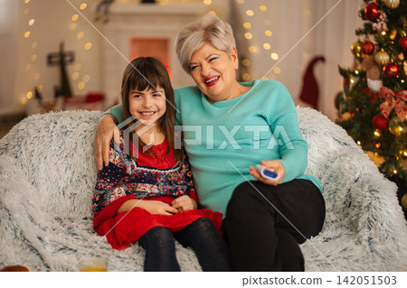 Grandmother and granddaughter watching television laughing together at Christmas Grandmother and granddaughter watching television laughing together at Christmas 142051503