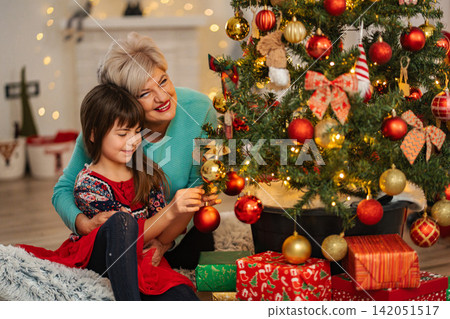Grandmother and granddaughter decorating Christmas tree together Grandmother and granddaughter decorating Christmas tree together 142051517