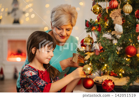 Grandmother and granddaughter decorating Christmas tree for holidays Grandmother and granddaughter decorating Christmas tree for holidays 142051519