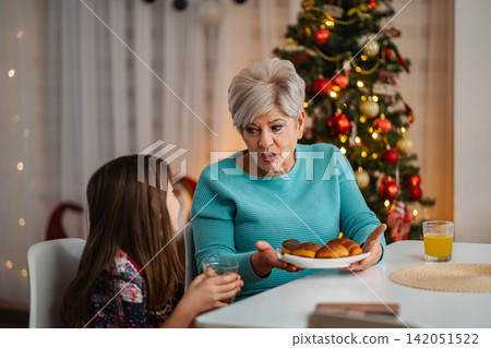Grandmother surprising granddaughter with pastry at Christmas Grandmother surprising granddaughter with pastry at Christmas 142051522