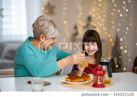Grandmother and granddaughter sharing breakfast drinking orange juice Grandmother and granddaughter sharing breakfast drinking orange juice 142051526