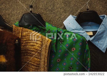 Fashion still life featuring a green patterned blouse, mustard knit sweater and embellished blue shirt on hangers, blending vintage style, bold colors, texture and eclectic autumn fashion trends now! Fashion still life featuring a green patterned blouse, mustard knit sweater and embellished blue shirt on hangers, blending vintage style, bold colors, texture and eclectic autumn fashion trends now! 142053022