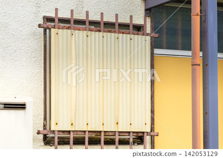 Iron bars and corrugated sheeting on the windows of an old house. Iron bars and corrugated sheeting on the windows of an old house. 142053129