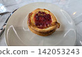 Golden flaky danish pastry jam tart puff served on a white plate with a fork on a marble table, ideal for breakfast, brunch, or dessert photography. Warm, homemade, sweet and appetizing bakery 142053243