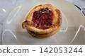 Golden flaky danish pastry jam tart puff served on a white plate with a fork on a marble table, ideal for breakfast, brunch, or dessert photography. Warm, homemade, sweet and appetizing bakery 142053244