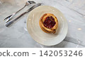 Golden flaky danish pastry jam tart puff served on a white plate with a fork on a marble table, ideal for breakfast, brunch, or dessert photography. Warm, homemade, sweet and appetizing bakery 142053246
