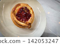 Golden flaky danish pastry jam tart puff served on a white plate with a fork on a marble table, ideal for breakfast, brunch, or dessert photography. Warm, homemade, sweet and appetizing bakery 142053247