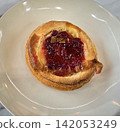 Golden flaky danish pastry jam tart puff served on a white plate with a fork on a marble table, ideal for breakfast, brunch, or dessert photography. Warm, homemade, sweet and appetizing bakery 142053249