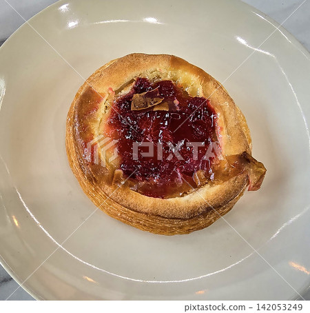 Golden flaky danish pastry jam tart puff served on a white plate with a fork on a marble table, ideal for breakfast, brunch, or dessert photography. Warm, homemade, sweet and appetizing bakery 142053249