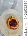 Golden flaky danish pastry jam tart puff served on a white plate with a fork on a marble table, ideal for breakfast, brunch, or dessert photography. Warm, homemade, sweet and appetizing bakery 142053250