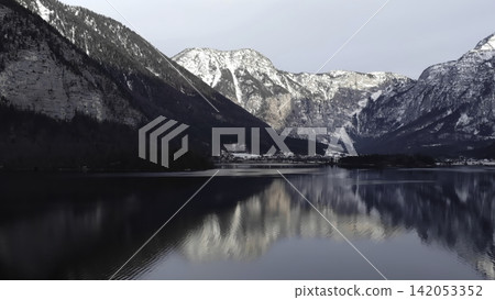 Calm Icy Lake Reflecting Mountain Village. Peaceful Frozen Lake Mirrors Snowcovered Town And Cliffs. Media Calm Icy Lake Reflecting Mountain Village. Peaceful Frozen Lake Mirrors Snowcovered Town And Cliffs. Media 142053352