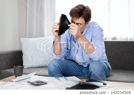 Stressed man looks into an empty wallet, struggling with unpaid utility bills, rising heating expenses, and financial crisis due to inflation. Stressed man looks into an empty wallet, struggling with unpaid utility bills, rising heating expenses, and financial crisis due to inflation. 142054308