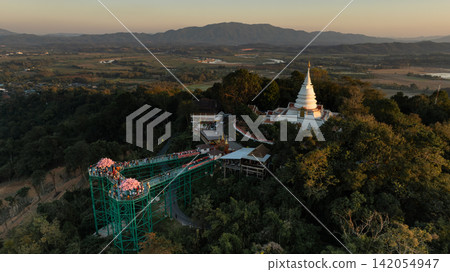 Aerial view of Phra Borommathat Phutthanimit Chedi and skywalk at Wat Phrathat Pha Ngao. The temple complex rises above the forested hillside. Aerial view of Phra Borommathat Phutthanimit Chedi and skywalk at Wat Phrathat Pha Ngao. The temple complex rises above the forested hillside. 142054947