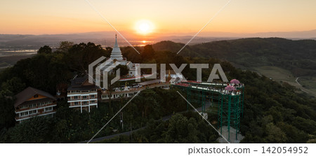 Aerial view of the temple and skywalk during sunset. The elevated complex is framed by forest, hills, and evening light. Aerial view of the temple and skywalk during sunset. The elevated complex is framed by forest, hills, and evening light. 142054952