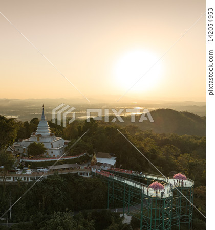 Aerial view of the temple and skywalk during sunset. The elevated complex is framed by forest, hills, and evening light. Aerial view of the temple and skywalk during sunset. The elevated complex is framed by forest, hills, and evening light. 142054953