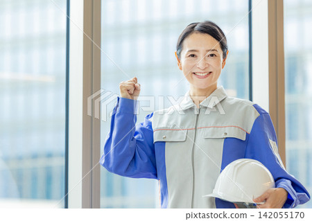 Woman in work clothes holding a helmet Woman in work clothes holding a helmet 142055170