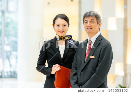 經理和女員工站在飯店大廳裡。 經理和女員工站在飯店大廳裡。 142055192