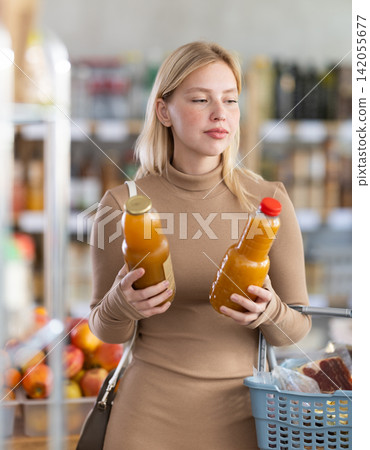 Girl buyer examine goods, choose peach juice in store Girl buyer examine goods, choose peach juice in store 142055677