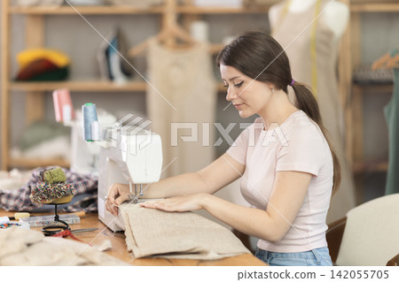 Seamstress working on modern sewing machine in sewing workshop Seamstress working on modern sewing machine in sewing workshop 142055705