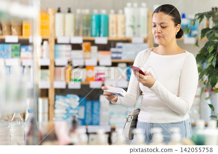 Middle-aged woman customer scanning QR-code on ointment in drugstore Middle-aged woman customer scanning QR-code on ointment in drugstore 142055758