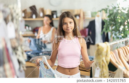 Happy teenage girl choosing something for summer in clothing store Happy teenage girl choosing something for summer in clothing store 142055765