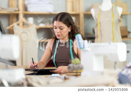 Female seamstress designing custom dress using tablet in studio Female seamstress designing custom dress using tablet in studio 142055806