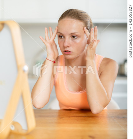 Attentive teenage girl looking at her face in mirror in kitchen Attentive teenage girl looking at her face in mirror in kitchen 142055827