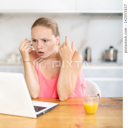 Teenage girl having problems with laptop while sitting at table in kitchen 142055837