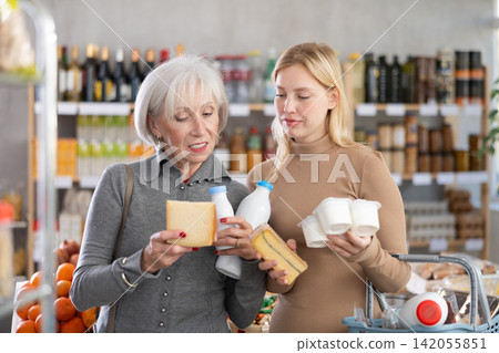 Girl and grandma with dairy products chooses something else, examines labels of cheese and yogurt Girl and grandma with dairy products chooses something else, examines labels of cheese and yogurt 142055851