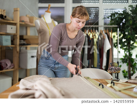 Female dressmaker using fabric shears to cut linen in workshop Female dressmaker using fabric shears to cut linen in workshop 142055959