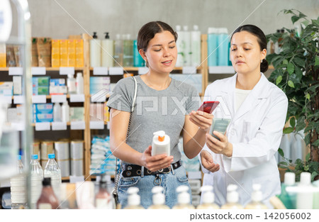Young girl scanning QR on cream while pharmacist offering in drugstore Young girl scanning QR on cream while pharmacist offering in drugstore 142056002