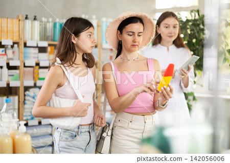 Interested mother and daughter selecting sunscreen cream or sun protection product in drugstore, woman pharmacist consulting customers Interested mother and daughter selecting sunscreen cream or sun protection product in drugstore, woman pharmacist consulting customers 142056006
