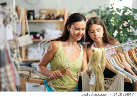 Near rack, daughter with mom buys something summer cloth, chooses items. Near rack, daughter with mom buys something summer cloth, chooses items. 142056047