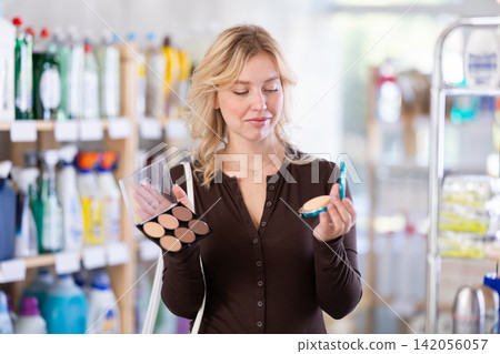 Girl housewife in cosmetic store examines goods, chooses eye shadow 142056057