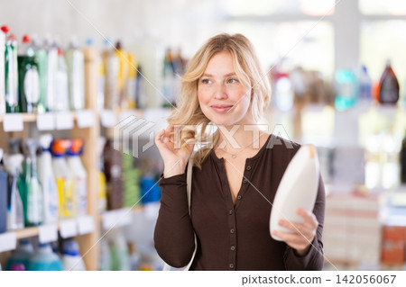 Girl housewife in household store examines goods, chooses hair care product Girl housewife in household store examines goods, chooses hair care product 142056067