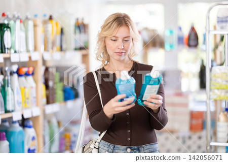 Girl housewife in household store examines goods, chooses mouthwash Girl housewife in household store examines goods, chooses mouthwash 142056071